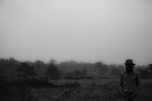 Persoon in landschap met hoed, zwart-wit foto.