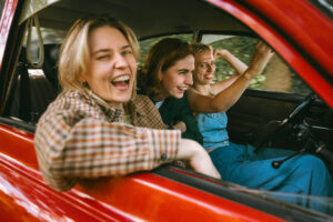 Drie vrienden lachen in een rijdende rode auto.