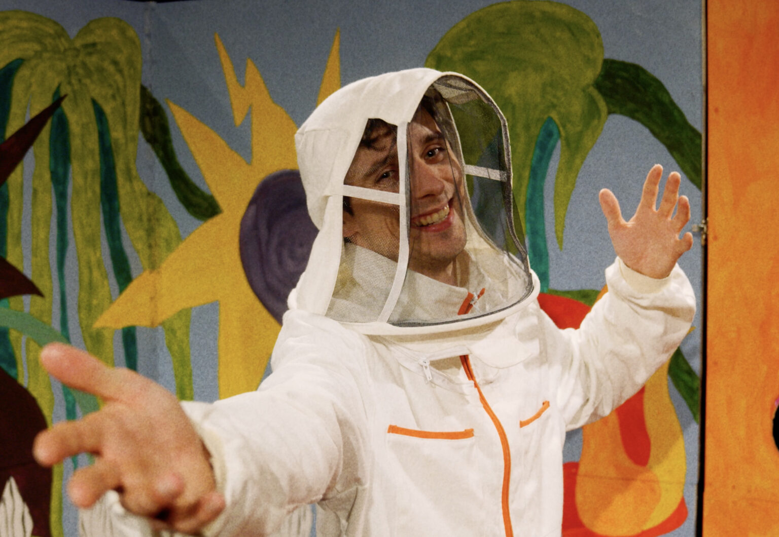 Man in astronautenpak zwaait vrolijk voor kleurrijke achtergrond.