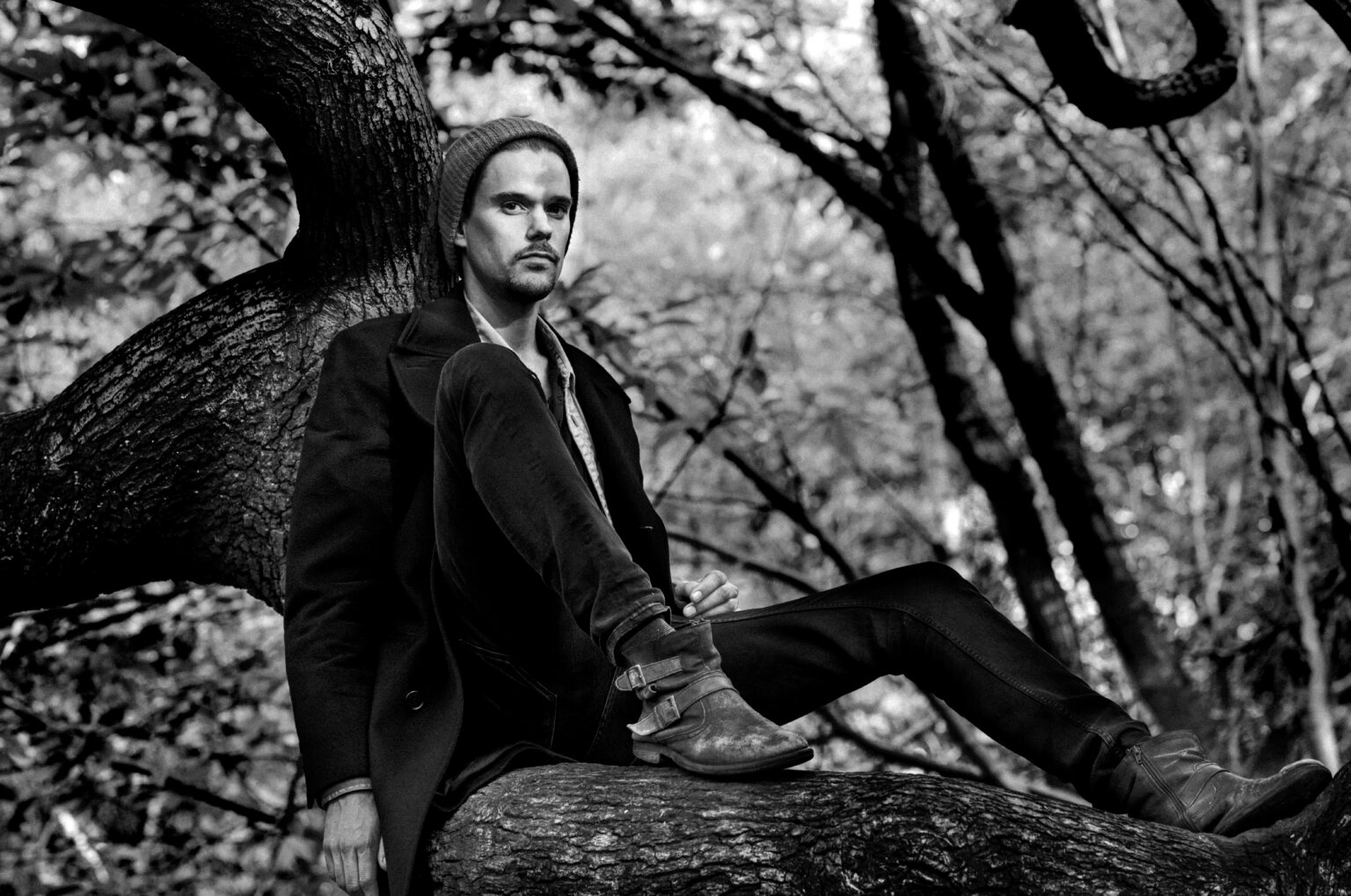 Man zit nadenkend op boomtak in bos, zwart-wit foto.