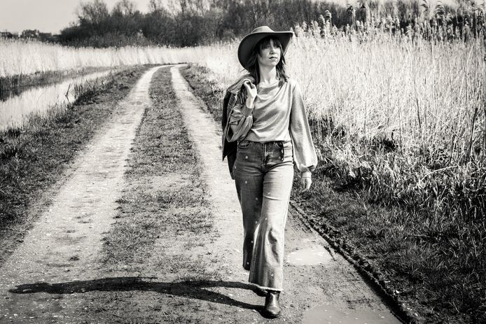 Vrouw wandelt op landweg tussen velden, zwart-witfoto.
