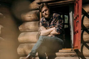 Man leunt in houten blokhutdeuropening.