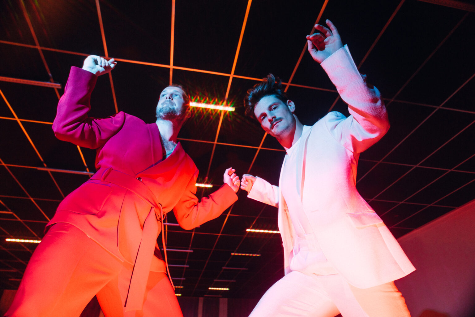 Twee mannen dansen in kleurrijke verlichte ruimte.