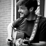 Man speelt gitaar buiten met glimlach.