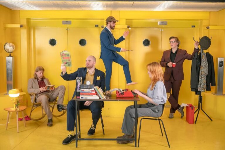 Groep mensen in geel ingerichte kamer met boeken.