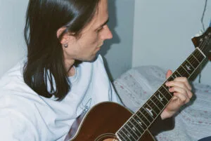 Persoon speelt gitaar op bed, relaxed moment thuis.