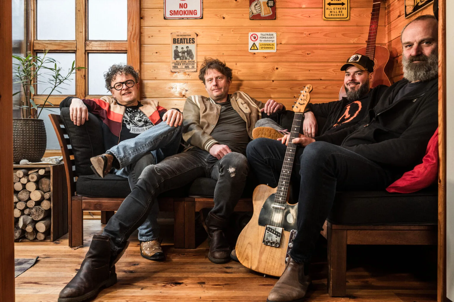 Vier mannen poseren met gitaar in houten kamer.