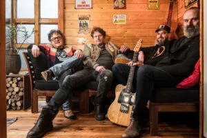Vier mannen poseren met gitaar in houten kamer.