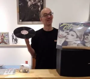 Man met vinylplaat en Blondie-album in winkel.