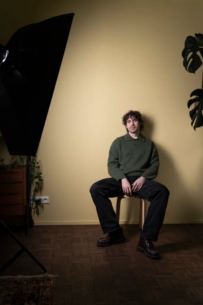 Man op stoel met groene trui in studio.