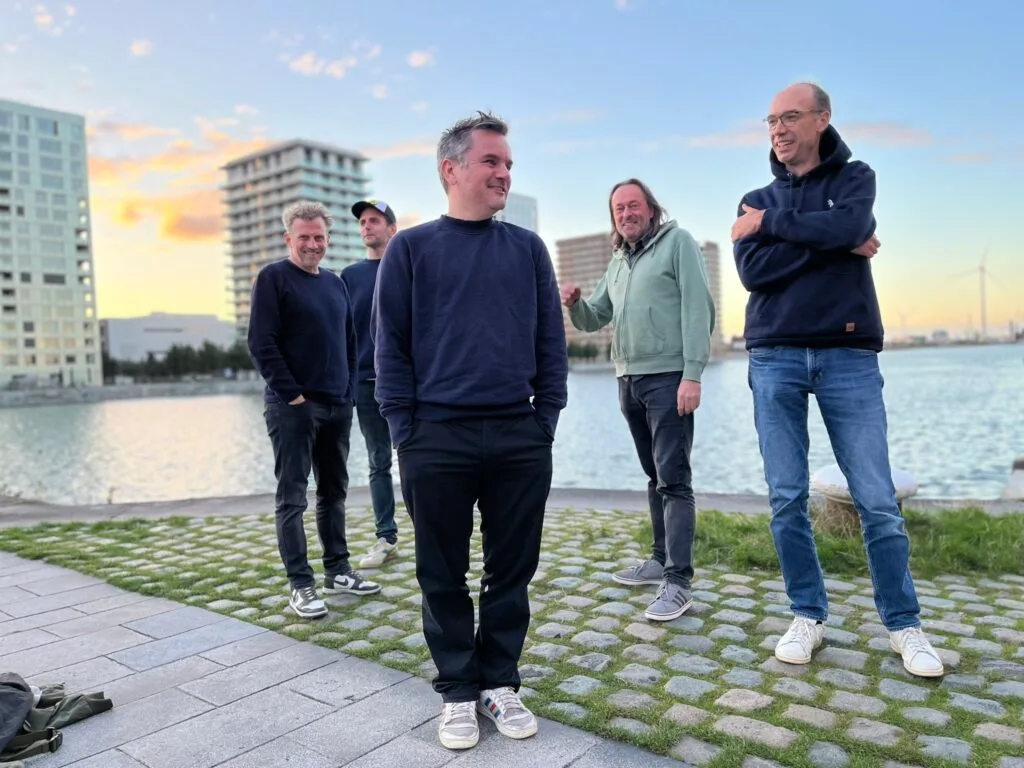 Vijf mannen poseren bij een rivier tijdens zonsondergang.