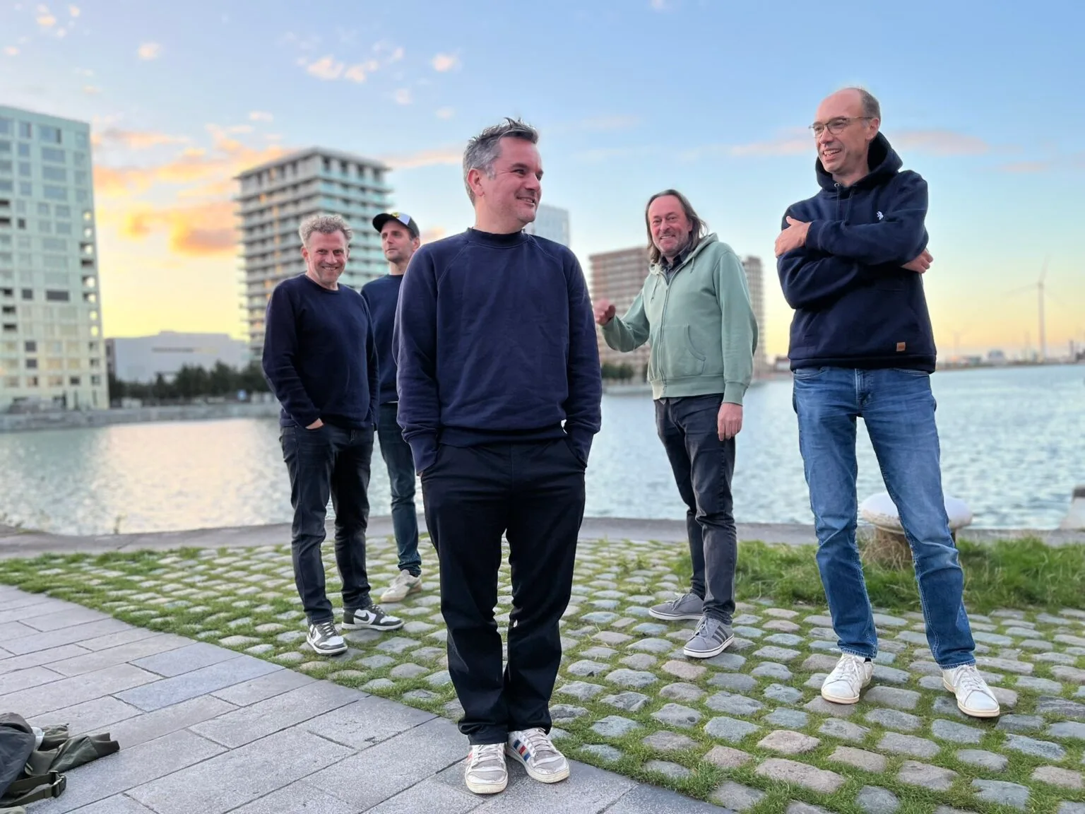 Vijf mannen poseren bij een rivier tijdens zonsondergang.