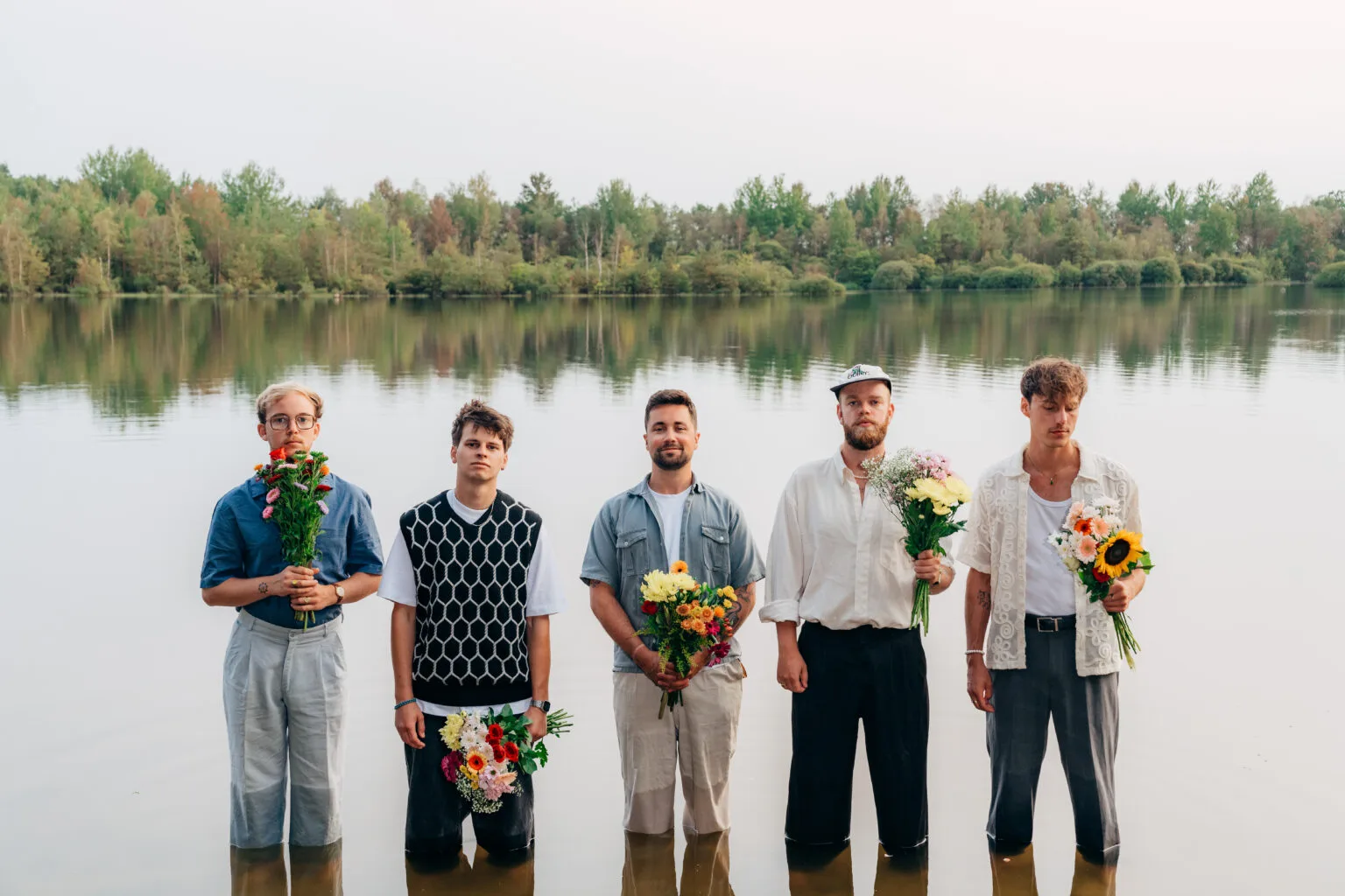 Vijf mannen met bloemen staan in water bij meer.