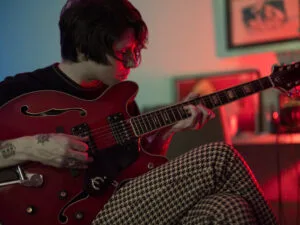 Persoon speelt elektrische gitaar in sfeervolle kamer.