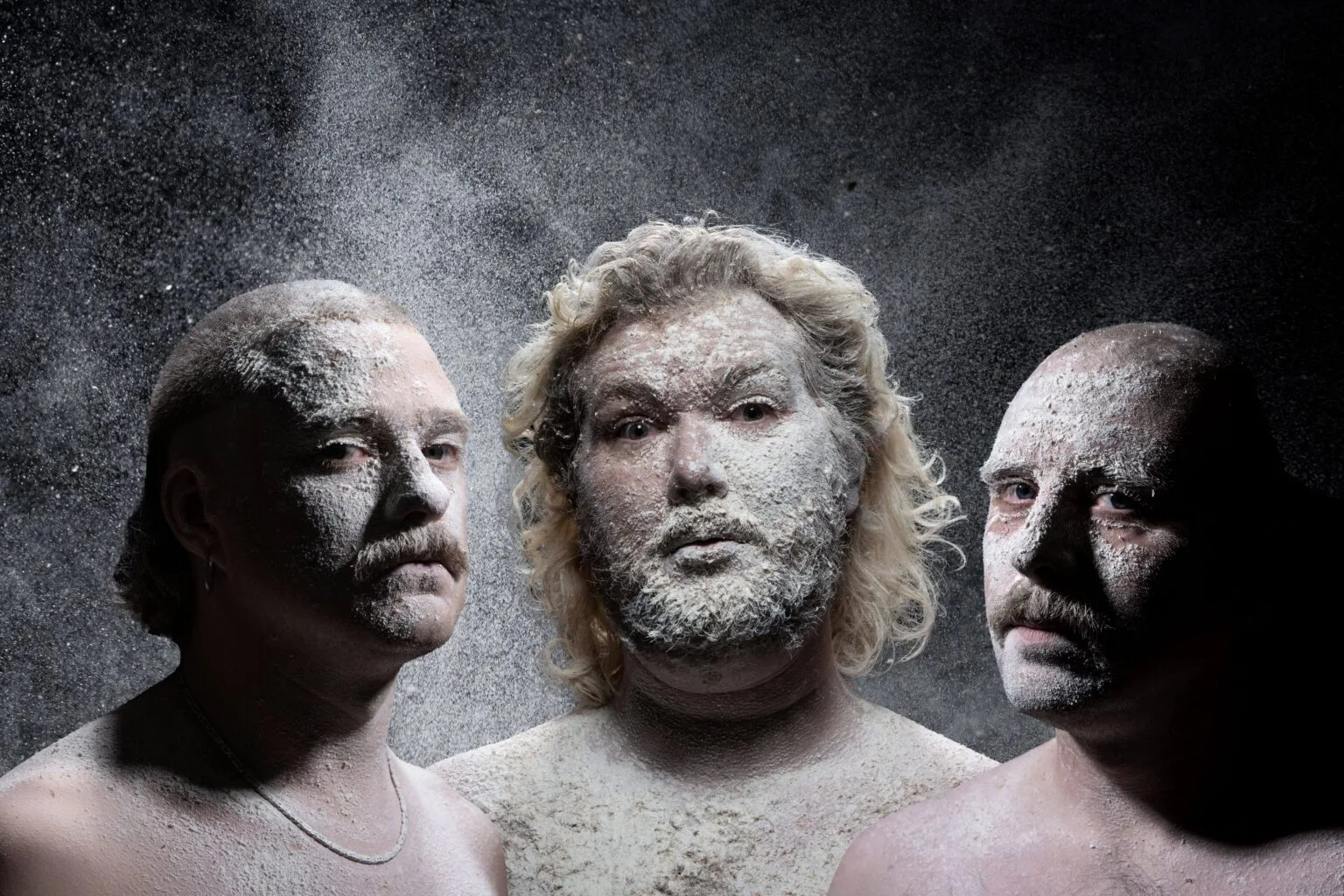 Drie mannen met poeder op gezichten, donkere achtergrond.