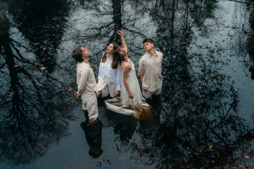 Vier mensen staan in reflecterend water, bosomgeving.