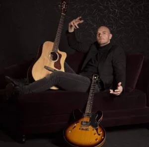 Man poseert met twee gitaren op bank