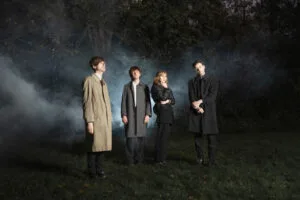 Vier mensen in een donkere, mistige buitenomgeving.