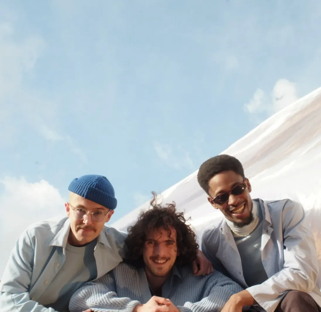 Drie mannen poseren buiten onder blauwe hemel.