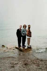 Drie mannen staan op rotsblok bij het water.